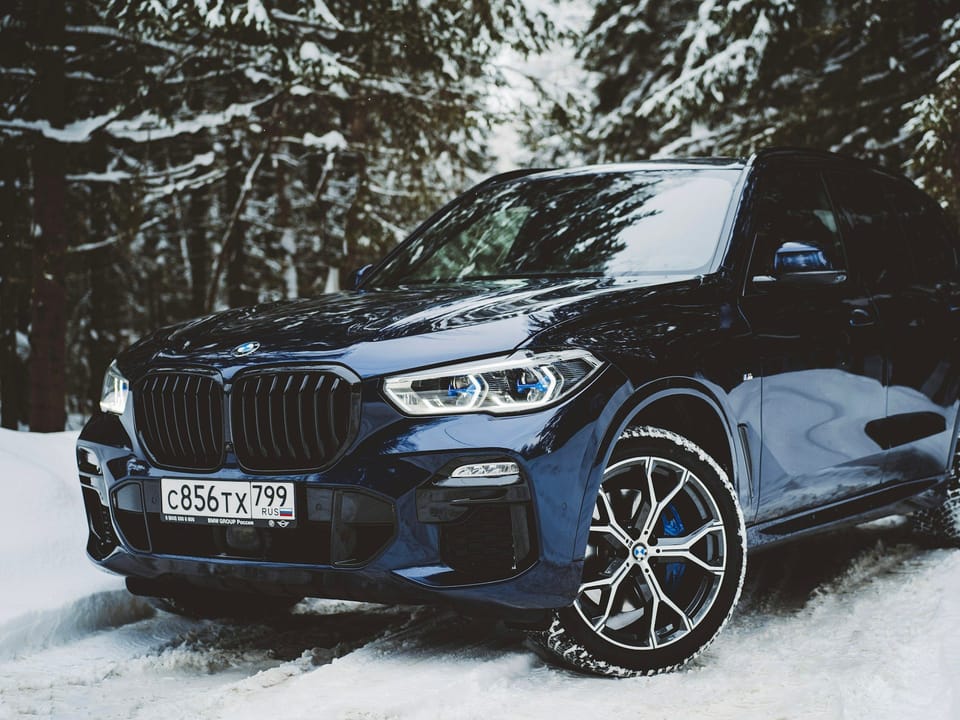 Синий BMW X5 на заснеженной дороге в лесу
